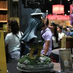 Life-size figure in a blue cloak and helmet standing on a rocky pedestal at a convention booth, with a The Lord of the Rings sign nearby.
