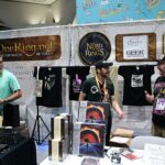 Convention booth for TheOneRing.net and The Nerd of the Rings with Tolkien-themed merch on display and staff present.