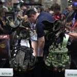Two detailed fantasy action figures displayed in a glass case, with rocky bases and price tags showing $279.99 and $299.99