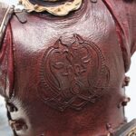 Close-up of a red leather breastplate with embossed decorative pattern and metallic trim, part of medieval armor.