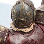 Close-up of ornate maroon and gold medieval armor with engraved panels and rivets.
