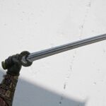 Close-up of a decorative sword with an ornate guard and leather-wrapped grip, held by a gloved hand against a white wall.
