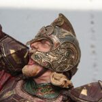 Close-up of a medieval knight statue in red and gold ornate armor, with a raised arm.