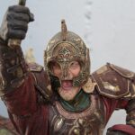 Close-up of a medieval-style armored statue raising its fist, with an ornate bronze helmet and richly detailed armor.