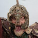 Close-up of a medieval warrior statue wearing an ornate bronze helmet with red gems and detailed engravings.
