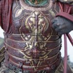 Close-up of ornate red and gold medieval armor on a torso, showcasing embossed patterns and belt details.
