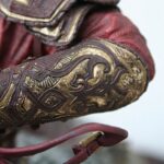 Close-up of ornate red and gold armor or costume detailing with intricate scrollwork patterns.