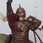 Figurine of a medieval knight in ornate red-bronze armor raising his right fist in triumph.