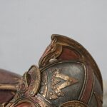Close-up of an ornate bronze helmet with intricate engravings and rivets.