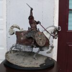 Decorative statue of a knight on an armored horse raising a sword in battle pose on a pedestal