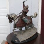 Statue of a armored knight on a prancing horse, sword raised above head, displayed on a pedestal outside a building.
