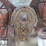 Close-up of an ornate brass keyhole lock embedded in carved reddish-brown wood panels with rivets and patterns.