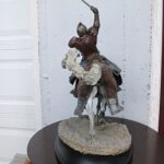 Mounted medieval knight statue raising a sword, on a rocky pedestal outdoors.
