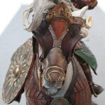 Close-up of a fantasy armored figure with decorative red-brown metal plates, rivets, and wing-like elements in the background.
