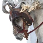 Close-up of a decorative horse statue wearing an ornate brown leather bridle and red reins, highlighting the sculpted mane and gear.