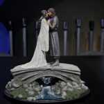 Diorama of a man and woman in medieval-style clothing standing close and facing each other on a rocky pedestal with a small waterfall beneath them.