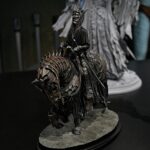 Dark armored fantasy figurine with a spiked helmet, standing on a rough stone pedestal in a dim display.
