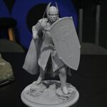 Gray-scale miniature of a medieval knight in armor, holding a long spear and a large shield, standing on a rocky base.