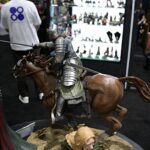 Armored knight on a rearing horse, wielding a spear in a convention display setting.