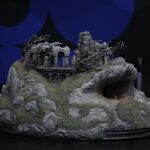 Miniature ruin sculpture with crumbling arches on a rocky base, set against a dark blue backdrop