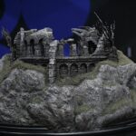 Detailed miniature ruins—stone arches and crumbling walls on a rocky, mossy base, with a dark background.