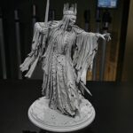 Grey statue of a crowned king with tattered flowing robes, sword raised, standing on a circular pedestal.