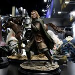Life-size Lord of the Rings figurines in armor and cloaks on a convention display table, with a horse statue in the background.