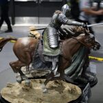 Armored knight on a rearing horse statue displayed on a rocky base, with caution tape in the background.
