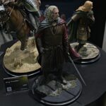Figure of King Theoden from Lord of the Rings, in medieval robes with cape, displayed on a rocky diorama at a convention.