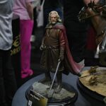 Detail shot of a King Theoden action figure in medieval armor with brown tunic and red cape on a display pedestal at a convention.