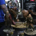 Lord of the Rings display figures: King Théoden on a horse with Éowyn nearby, showcased on a round pedestal at a convention with attendees in the background.
