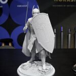 Gray knight statue with shield and spear, standing on rocky pedestal in a display case.