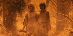 Two armored travelers walk through a frost-covered forest bathed in orange light; the front figure in plate armor holds a sword while a companion follows.
