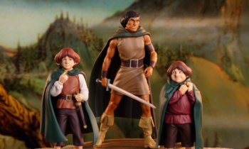 Aragorn with sword flanked by two Hobbit figures in cloaks on a rocky display against a fantasy landscape backdrop.