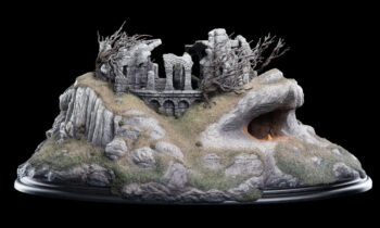 Scale model of a ruined stone castle on a rocky hill with a glowing cave entrance deep in the rock formation.