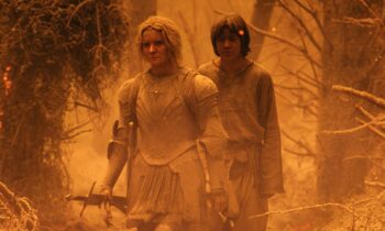 Two armored travelers walk through a frost-covered forest bathed in orange light; the front figure in plate armor holds a sword while a companion follows.